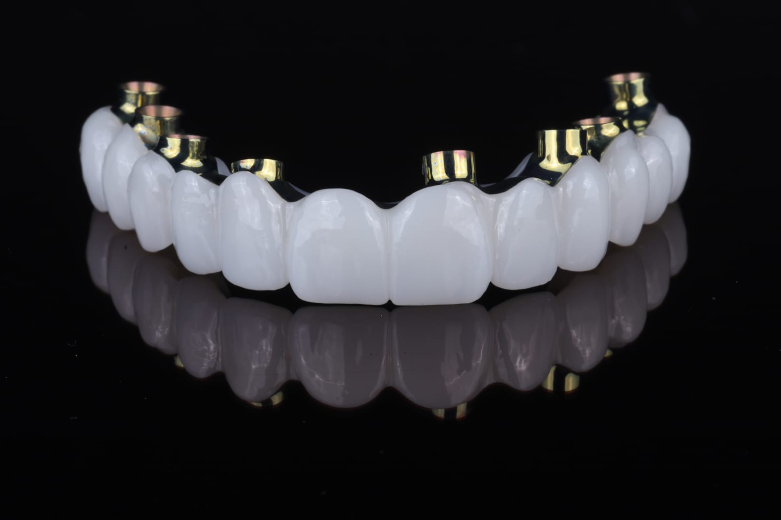 Monolithic zirconia implant supported fixed dental prosthesis photographed on black, with titanium abutment cylinders bonded into the screw channels.