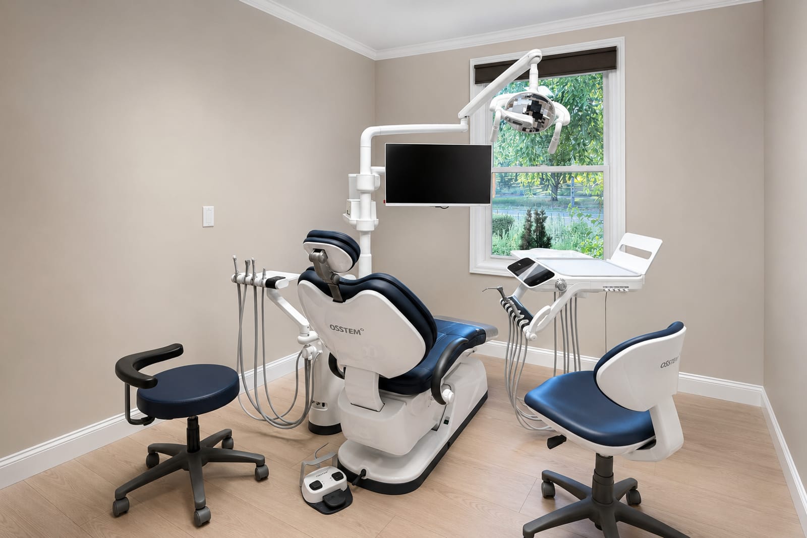 A navy Osstem treatment chair beside a window, with instrument tray and overhead light in a newly renovated operatory.