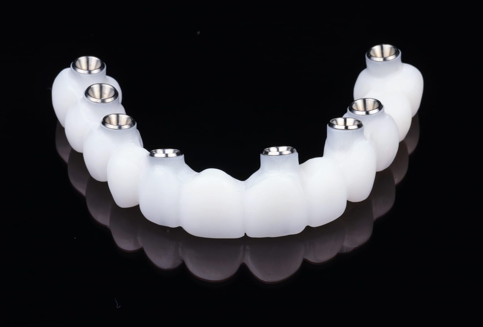 Provisional implant supported fixed dental prosthesis photographed on a black surface, showing titanium cylinders at the screw access positions.