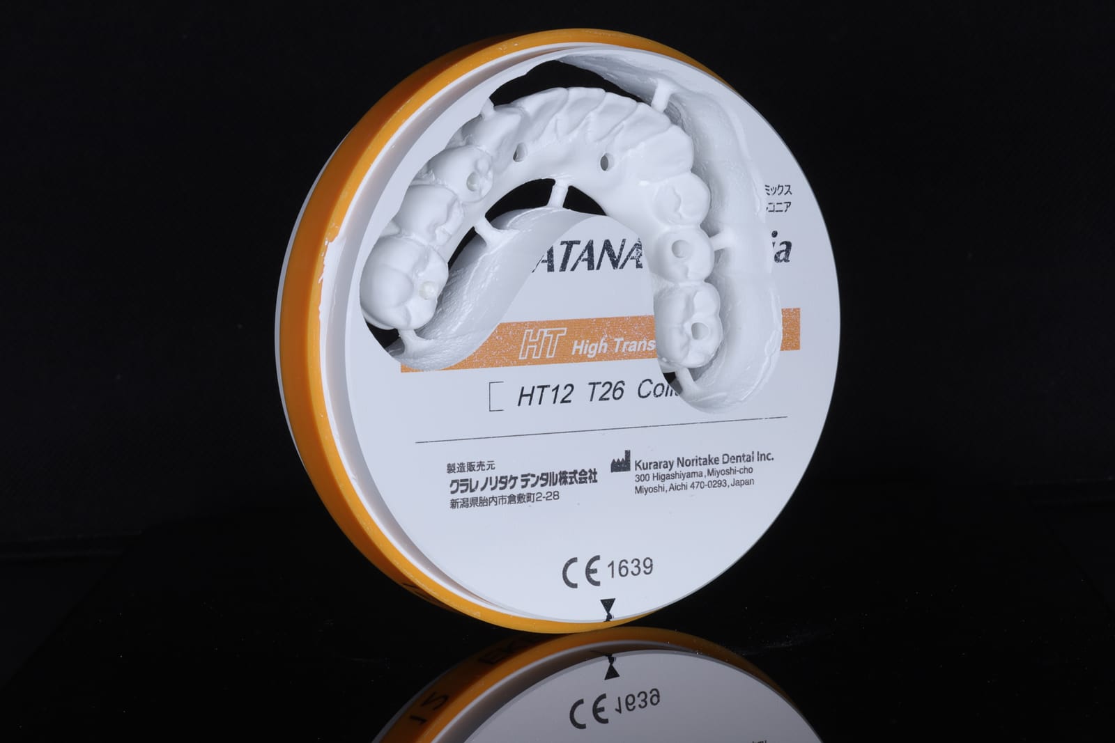 A zirconia milling disc standing on a black surface with a milled dental restoration held in the disc above it, the manufacturer marking visible across the face of the disc.